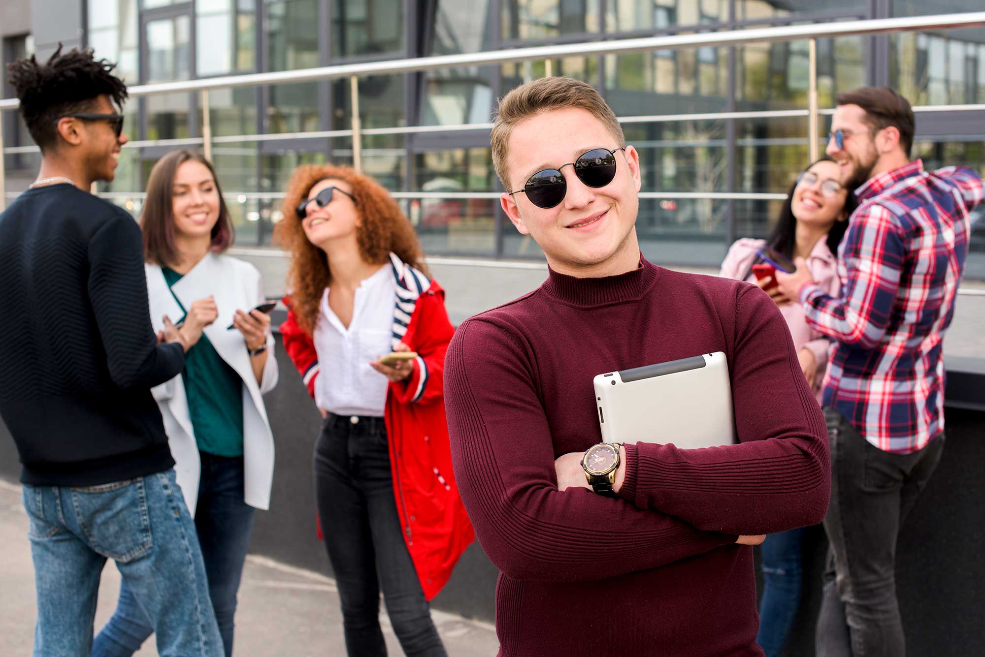 Student som står i solglasögon och tittar in i kameran, i omgiven av andra studenter